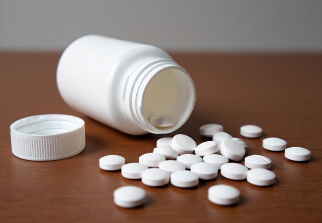 Белая баночка с таблетками лежит на деревянной поверхности